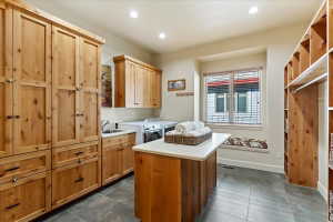 Spacious utility room featuring extensive natural wood cabinetry, a built-in sink, durable tile flooring, a functional center island with a light-colored countertop, and a window with a built-in bench