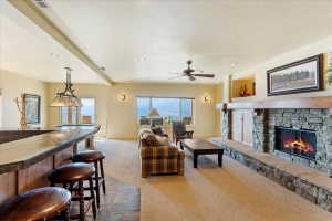 Spacious recreation room featuring a built-in bar with stone-finish countertop, a stone-faced fireplace with a wood mantel, recessed lighting, and a ceiling fan