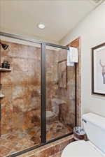 Glass-enclosed shower with a bronze frame, textured brown and rust-colored tile, built-in bench, and recessed lighting