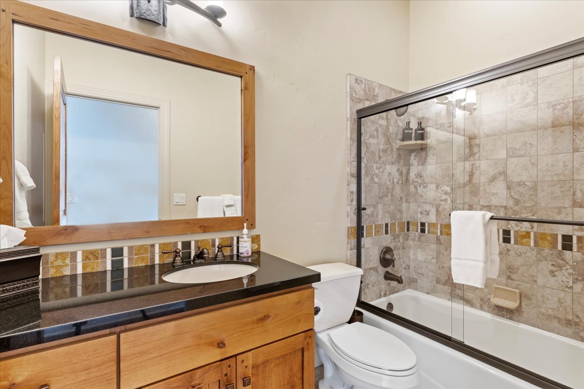 Bathroom featuring a wood-framed mirror, a dark countertop vanity with an undermount sink, and a tiled shower-tub combination with a glass enclosure