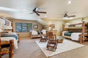 Spacious bedroom featuring neutral carpeting, multiple ceiling fans, and sloped ceilings with recessed lighting