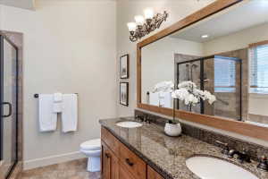 Spacious bathroom featuring a dual vanity with granite-style countertop, wood-finish cabinetry, a large framed mirror, and a glass-enclosed shower with tiled walls