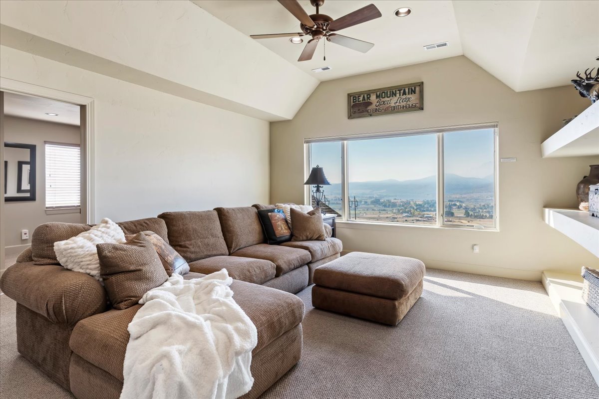 Spacious room featuring a large window with distant mountain and city scenery, vaulted ceilings, a ceiling fan, recessed lighting, and wall-mounted shelving