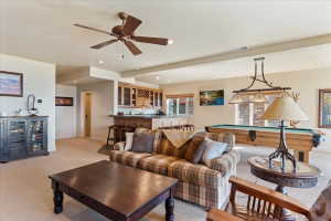 Open-concept recreation room featuring a built-in wet bar with wood cabinetry, a recessed bar area with pendant lighting, a ceiling fan, and carpeted flooring