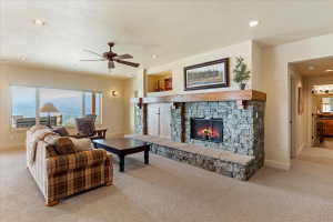 Spacious living area featuring a floor-to-ceiling stone fireplace with a substantial wood mantel, carpeted flooring, large picture windows, and recessed lighting