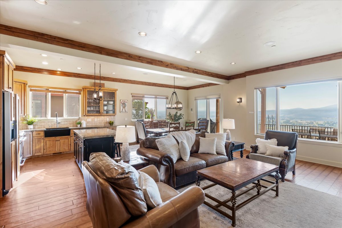 Open-concept living area with wood-finish flooring, exposed ceiling beams, recessed lighting, and expansive windows