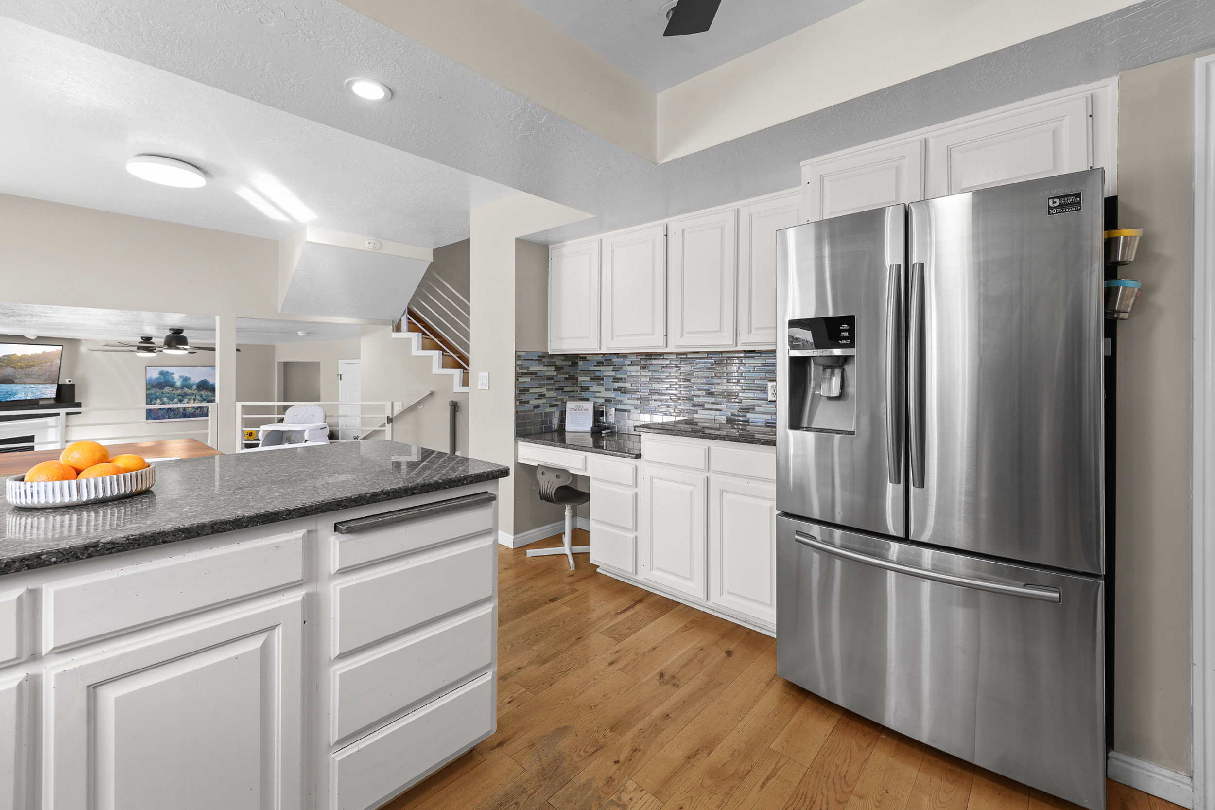 Modern kitchen featuring white cabinetry, a stainless steel French door refrigerator, a tiled backsplash, and wood-finish flooring