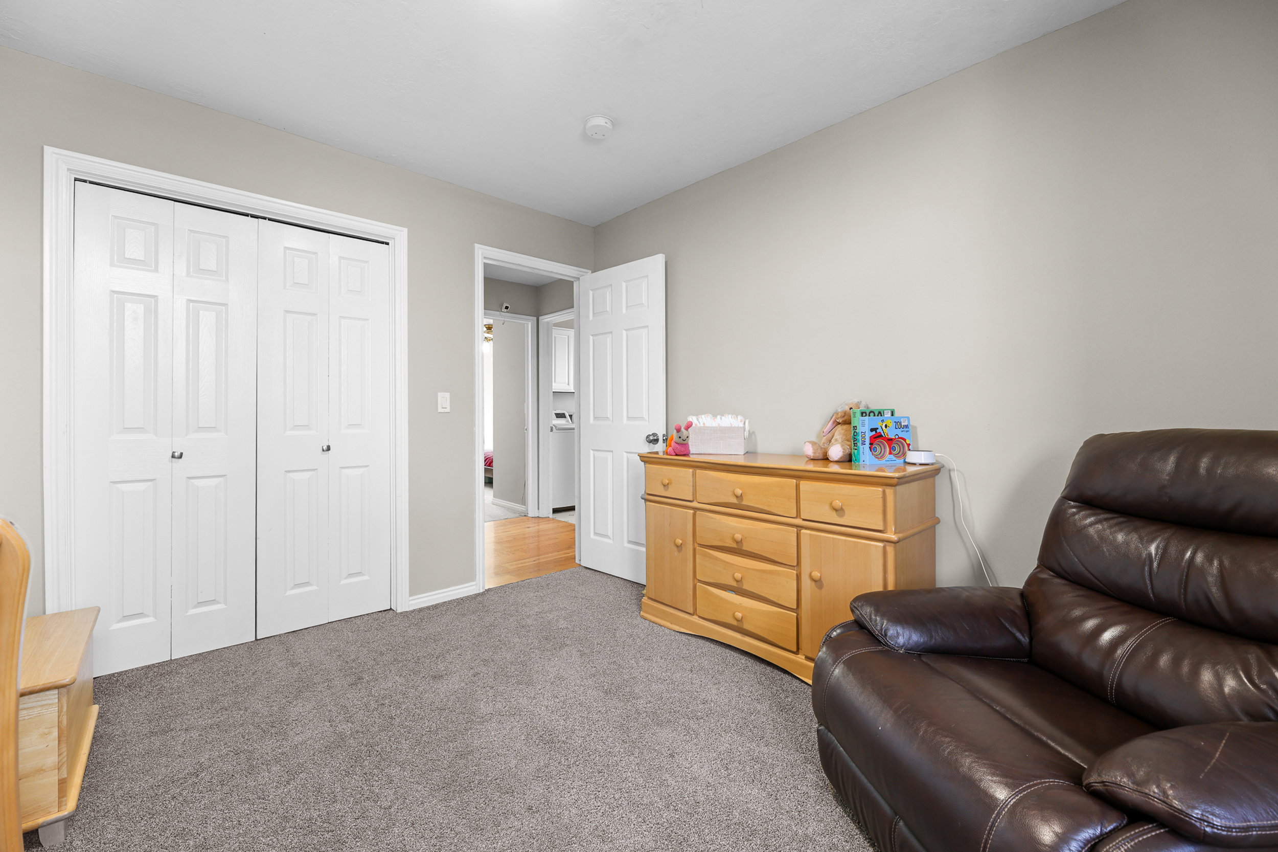 Interior room featuring neutral wall paint, gray carpeting, a built-in closet with bi-fold doors, and a doorway opening to another interior space with wood-finish flooring