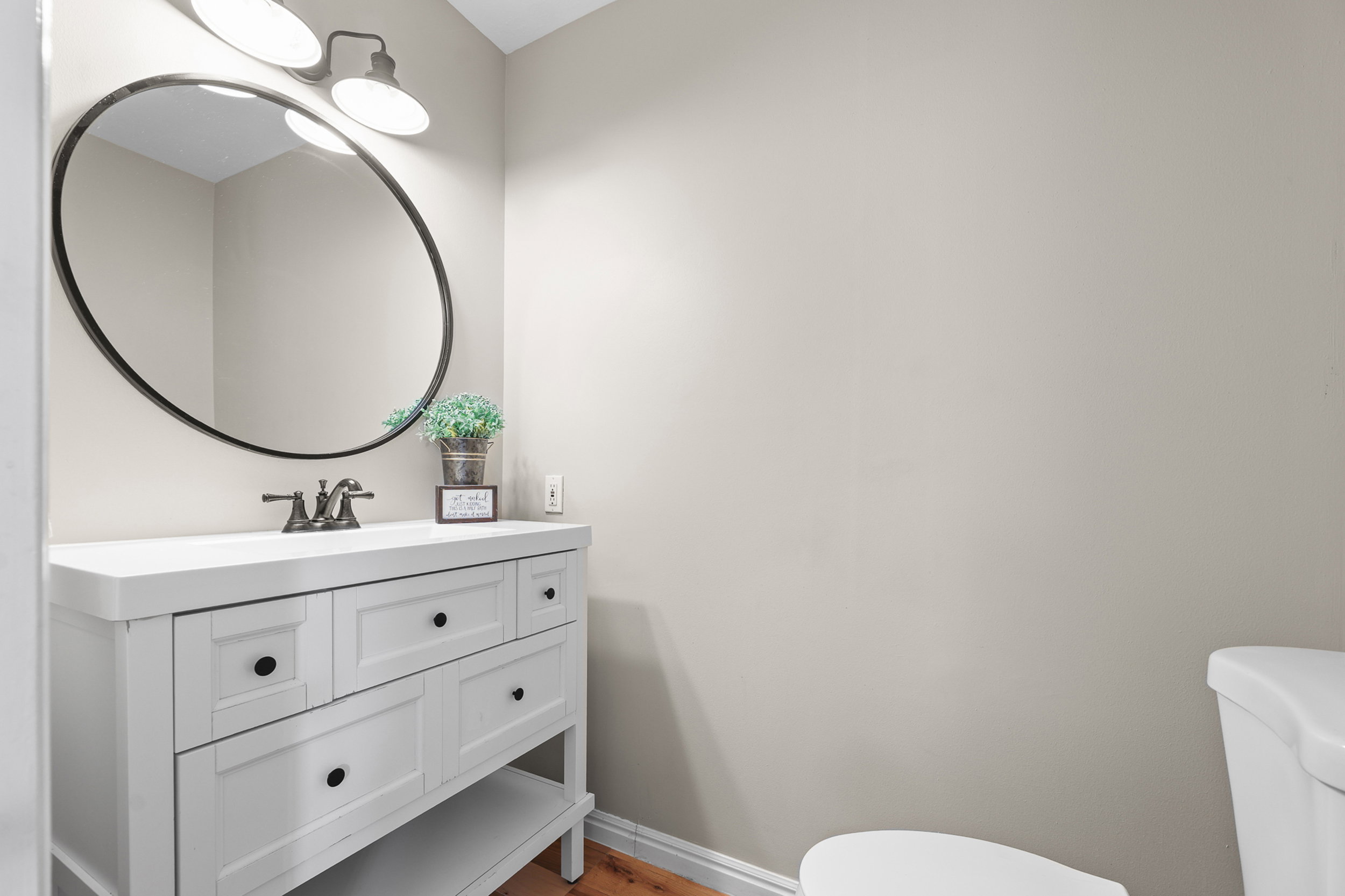 White vanity with black hardware, complementing a circular black-framed mirror and a three-light fixture