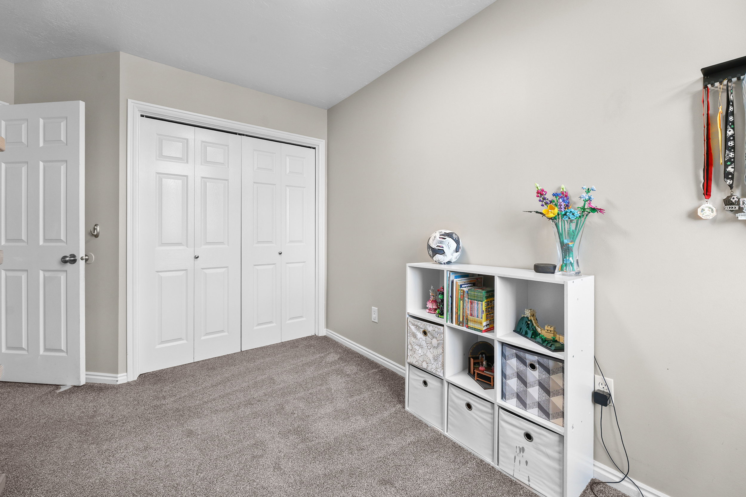 Neutral wall paint and grey carpeting define this room, featuring a white paneled door and double bifold closet doors