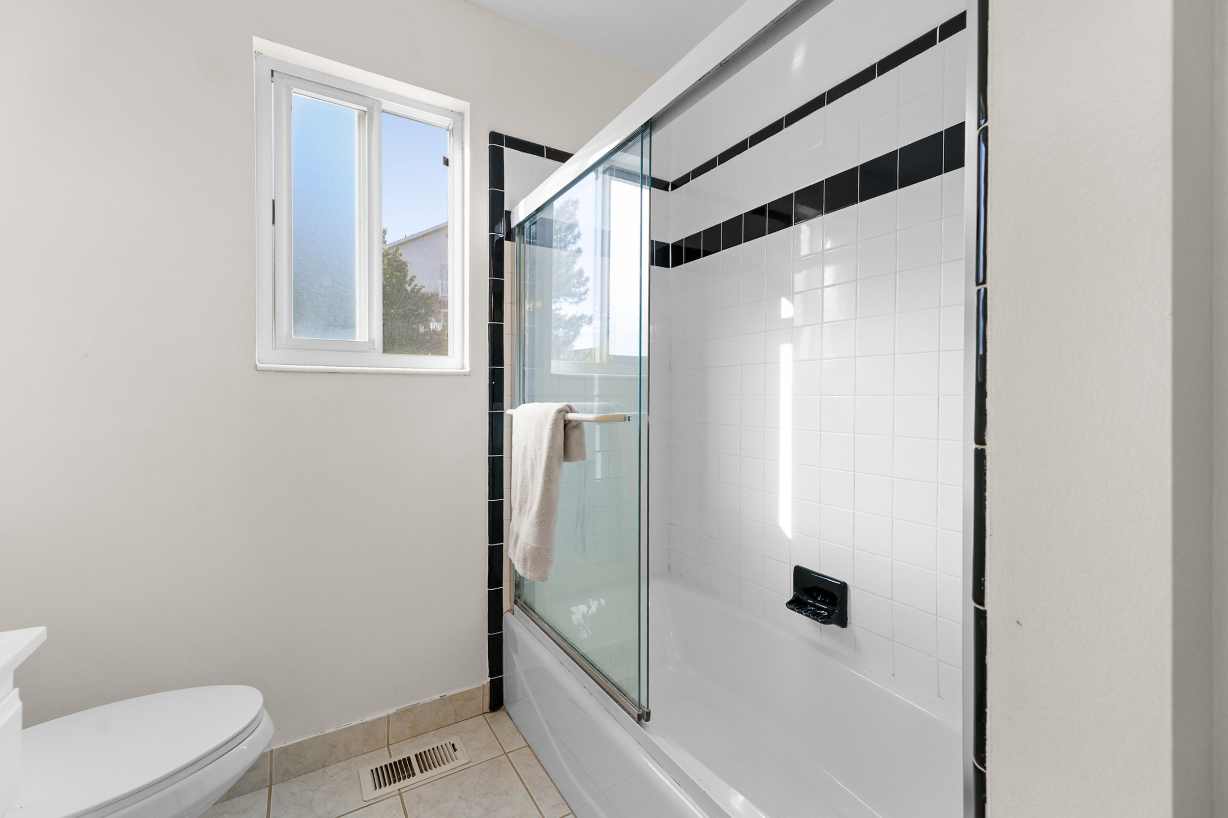 Bathtub with clear glass sliding door, white subway tile surround with black accent bands, and a modern dark-finish faucet