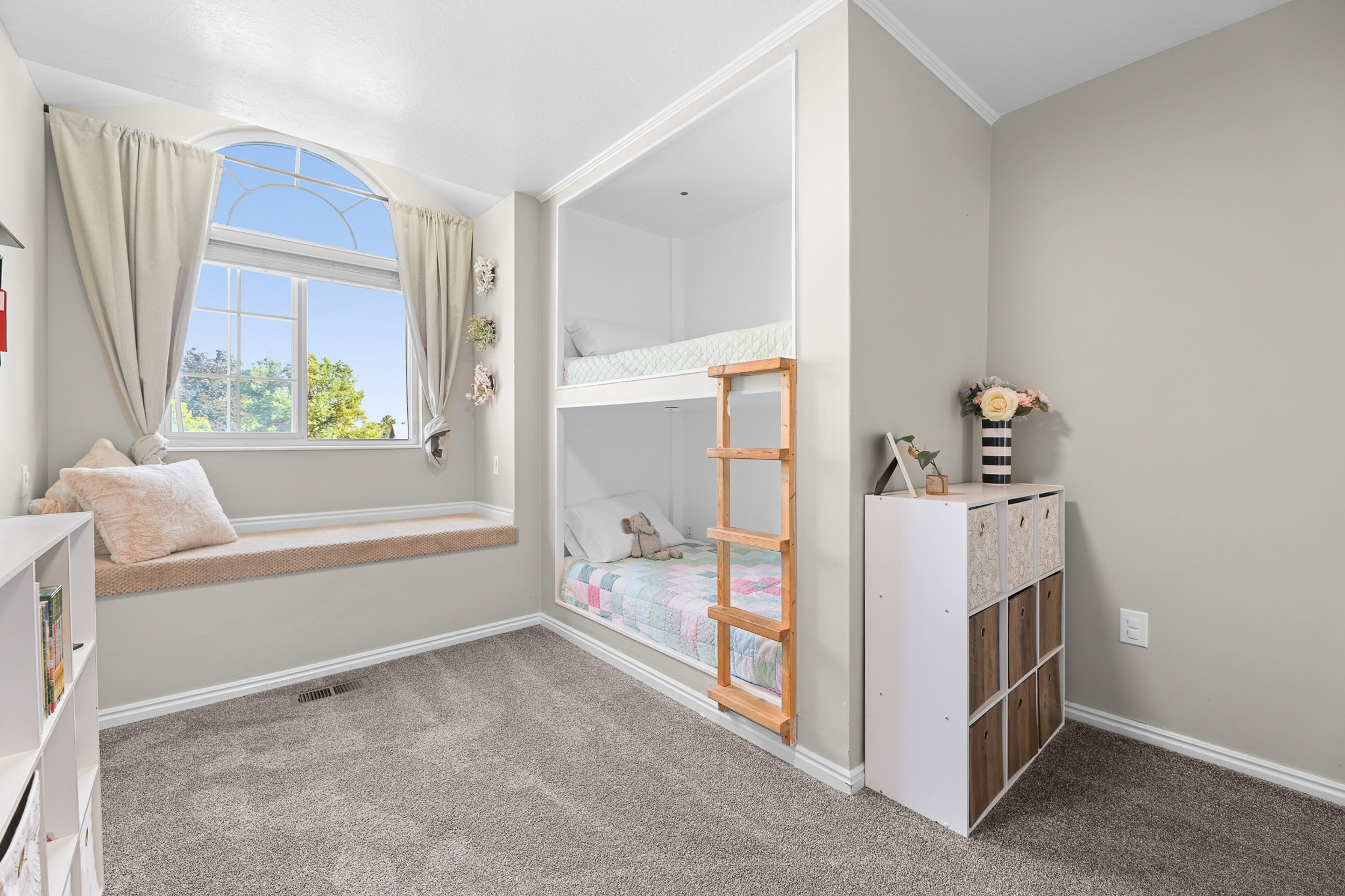Built-in bunk beds with a wooden ladder, arched window, and a window seat with a cushioned top