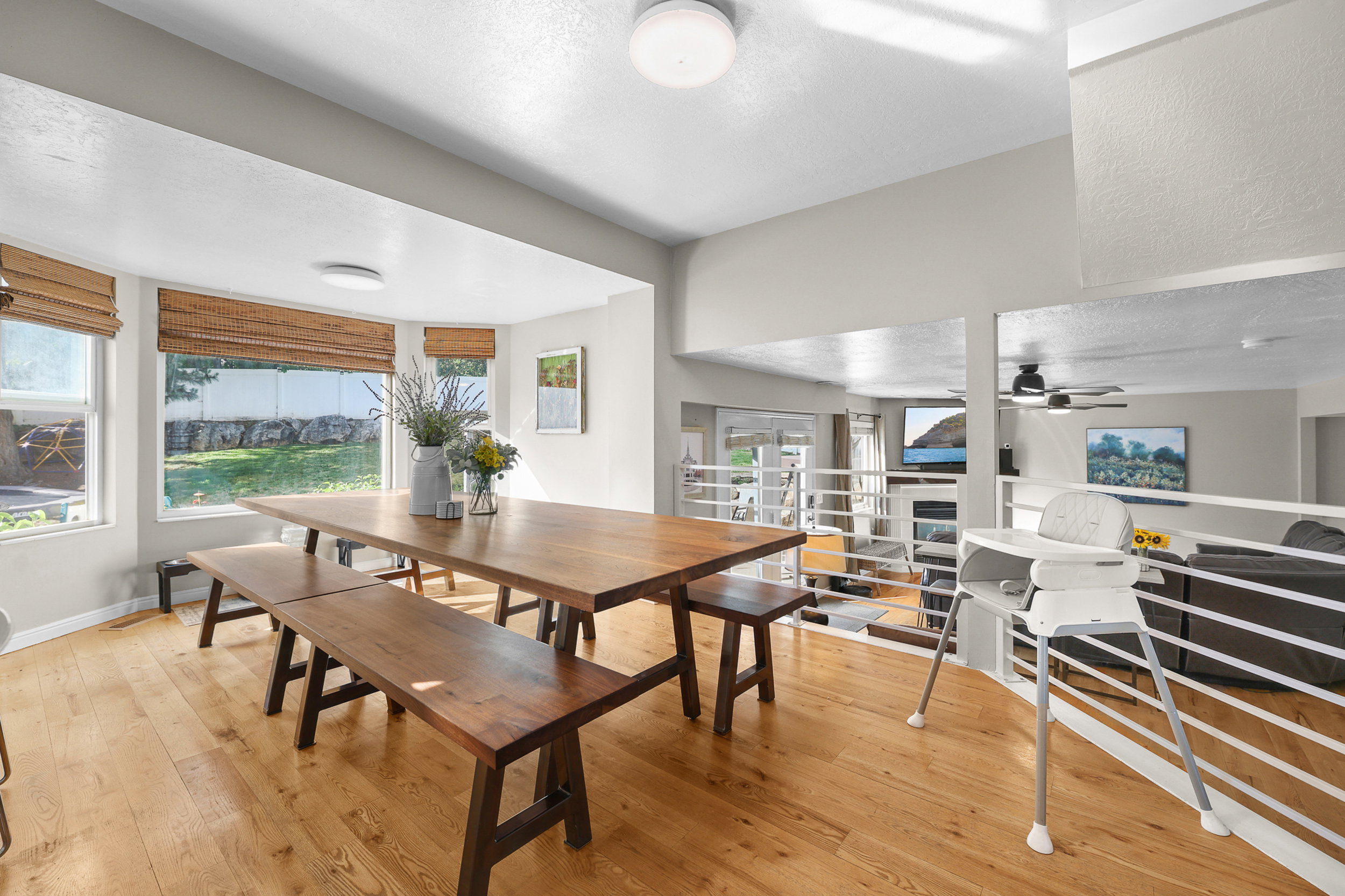 Spacious dining area featuring wood-finish flooring, ample natural light from multiple windows, and a semi-open design overlooking a lower-level living space