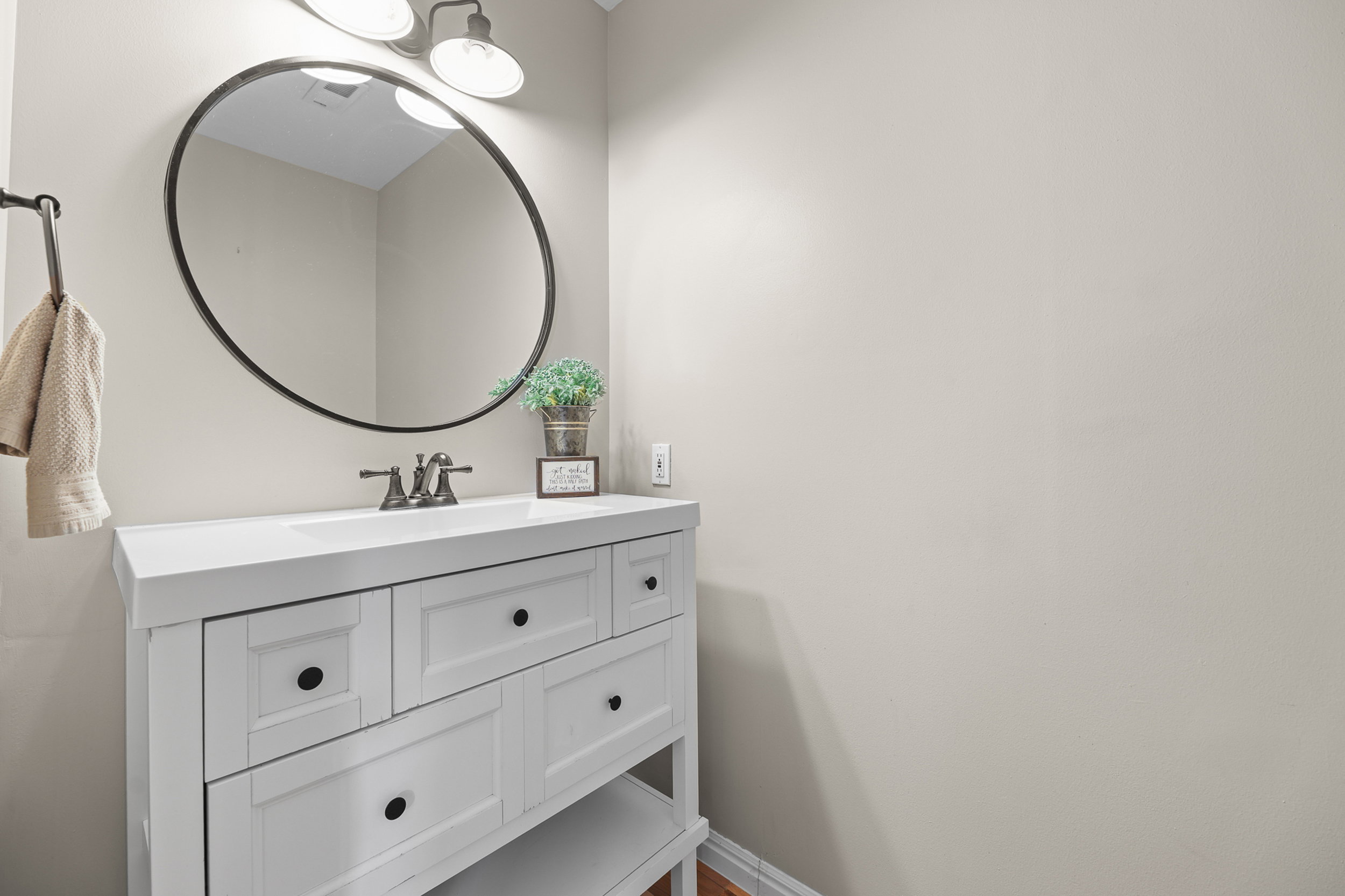 White vanity with integrated sink, black hardware, wall-mounted oval mirror with a black frame, and a two-light vanity fixture