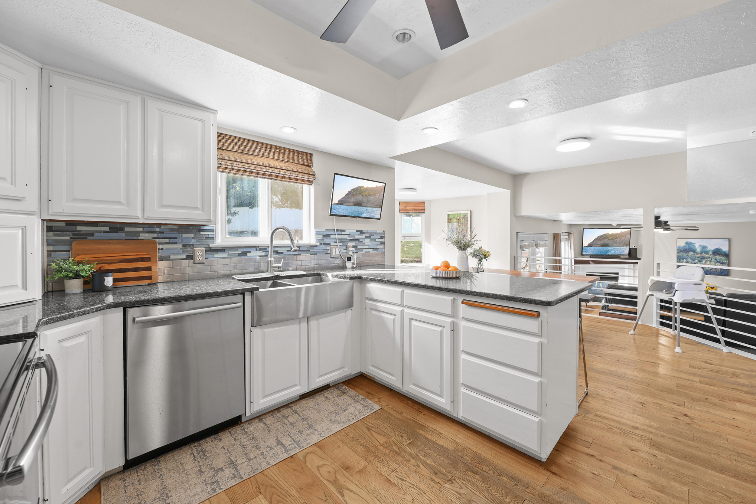Bright kitchen featuring white cabinetry, granite-style countertops, stainless steel appliances, a farmhouse sink with a gooseneck faucet, and wood-finish flooring