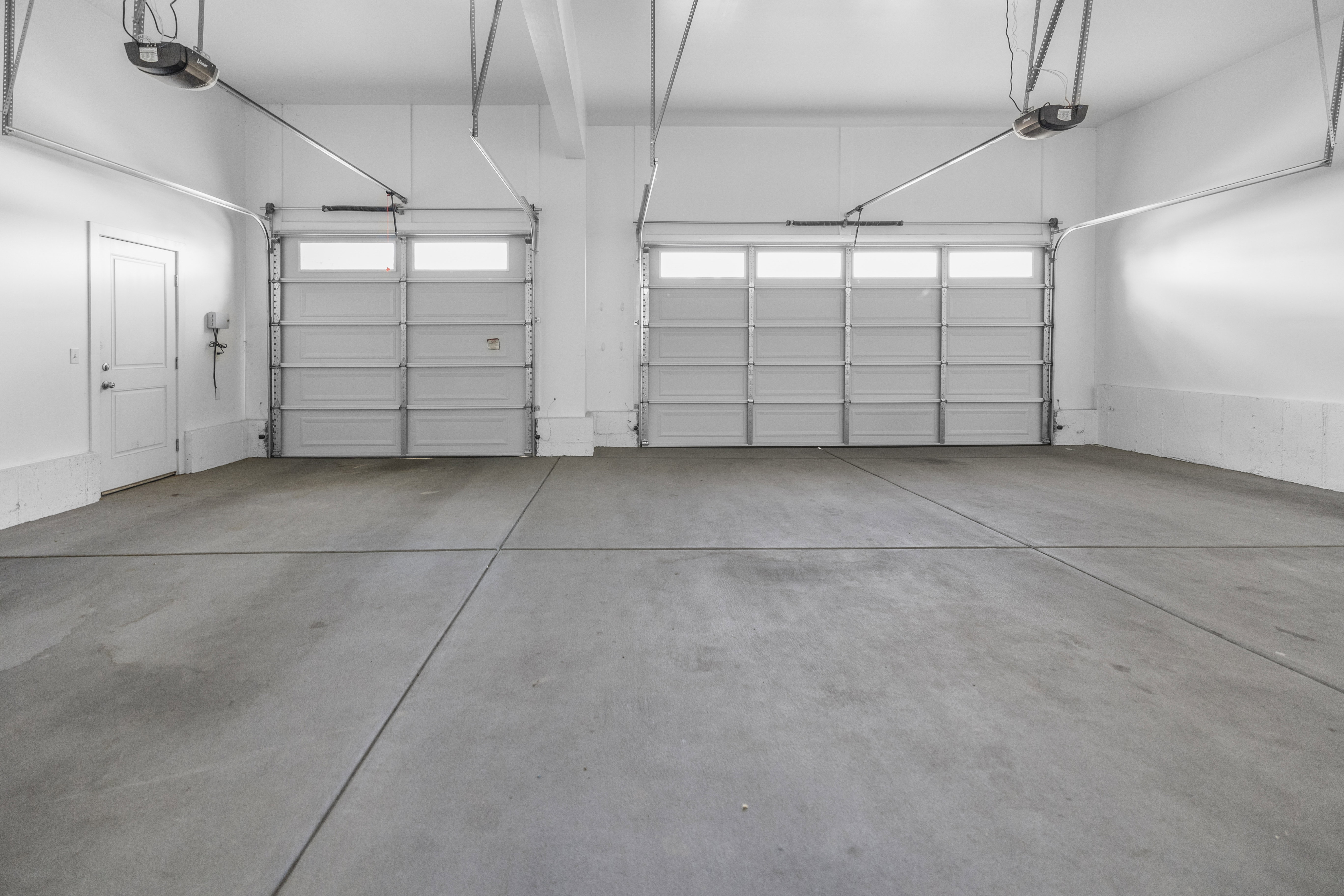 Spacious garage featuring two overhead doors with window panels, automatic openers, a pedestrian door, and painted concrete flooring