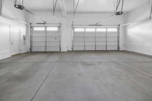 Spacious garage featuring two overhead doors with window panels, automatic openers, a pedestrian door, and painted concrete flooring
