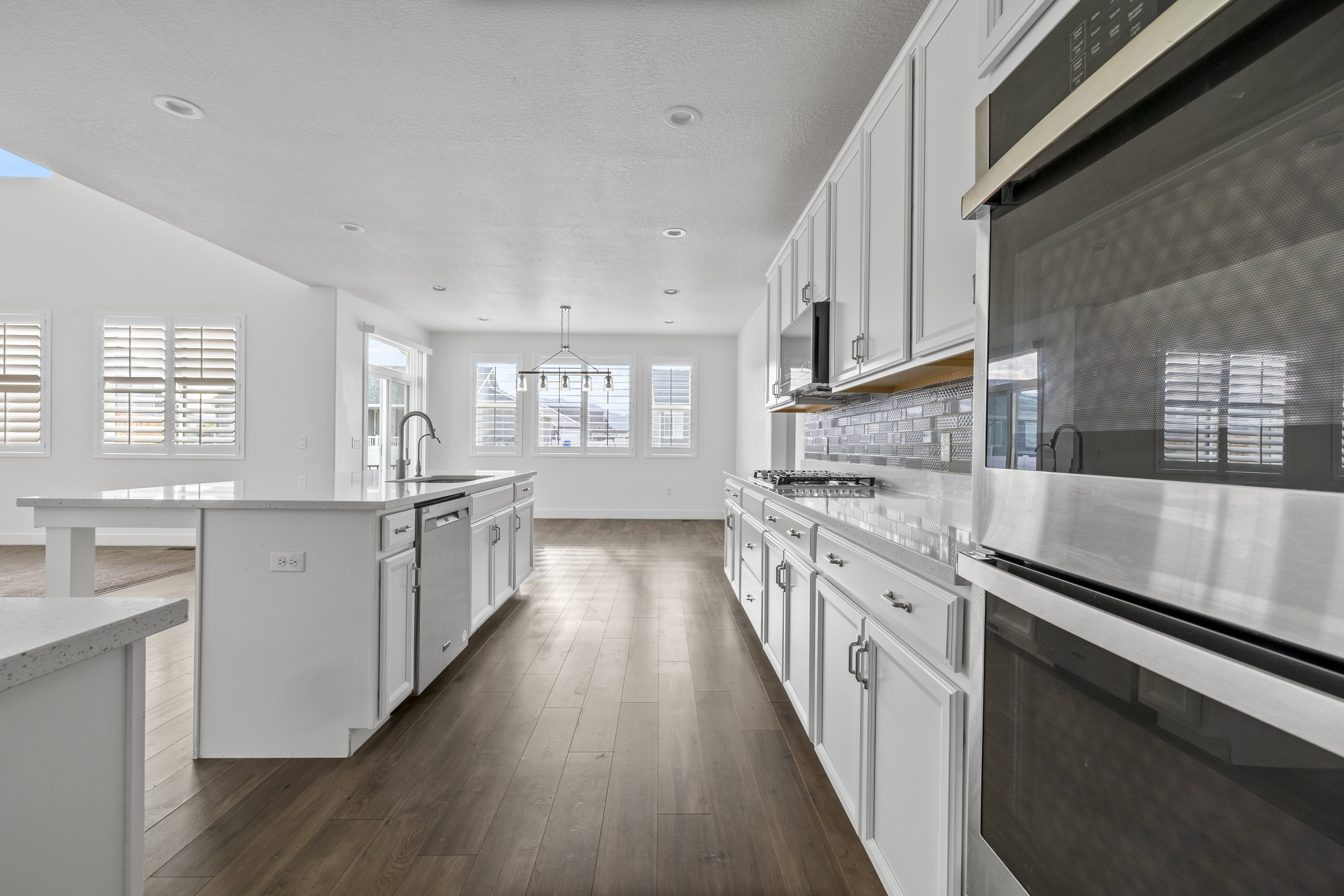 Modern kitchen featuring white cabinetry, stainless steel appliances, a center island with sink, quartz countertops, and wood-finish flooring