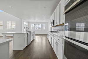 Modern kitchen featuring white cabinetry, stainless steel appliances, a center island with sink, quartz countertops, and wood-finish flooring
