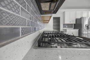 Built-in gas range with stainless steel finish, quartz-finish countertop, and patterned tile backsplash