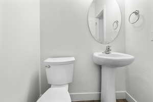 White pedestal sink with a chrome faucet, oval mirror, white toilet, and wood-finish flooring