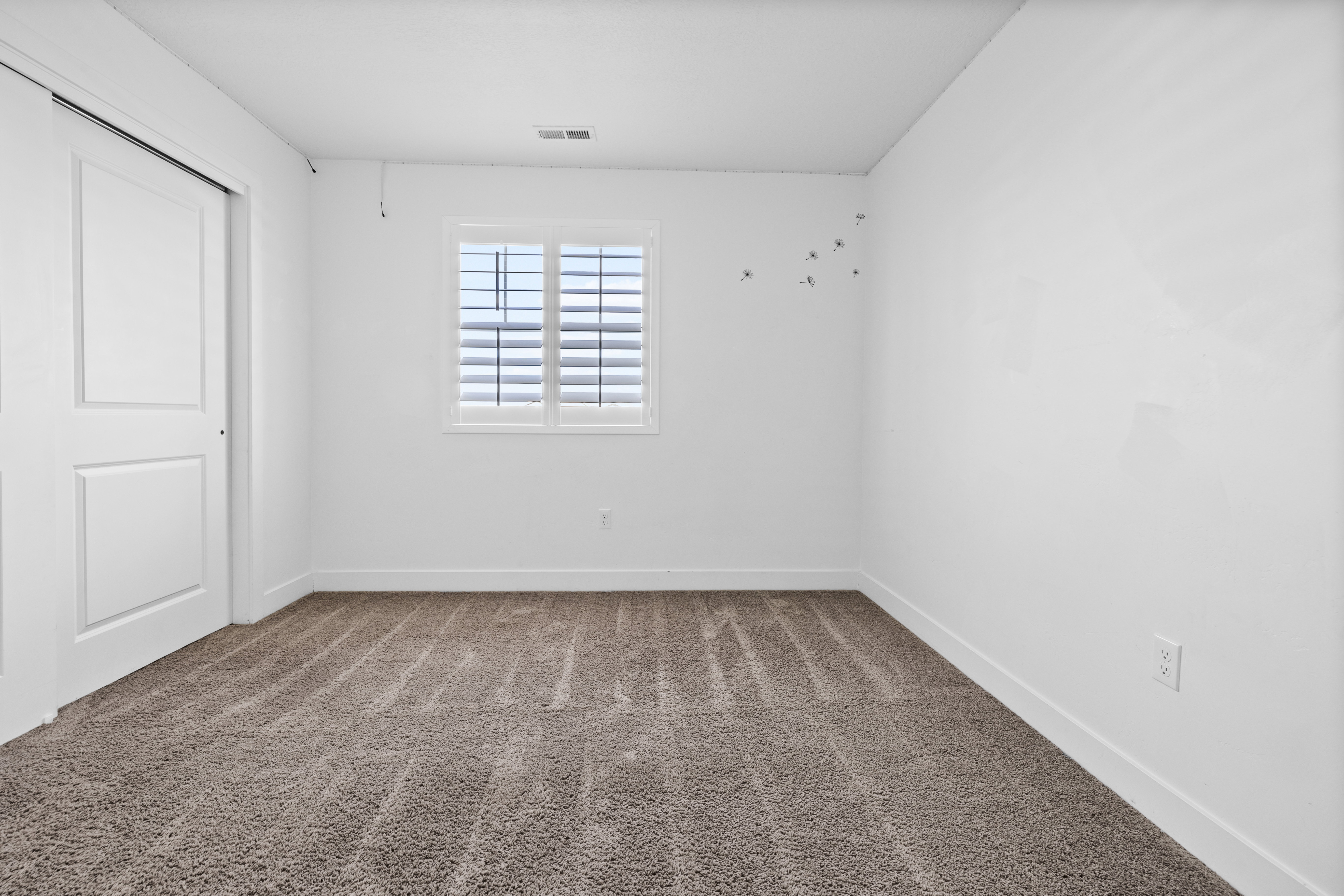 Bedroom 3 featuring neutral carpet flooring, white walls, a window with white plantation shutters, and a sliding panel door