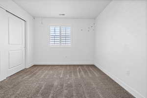 Bedroom 3 featuring neutral carpet flooring, white walls, a window with white plantation shutters, and a sliding panel door