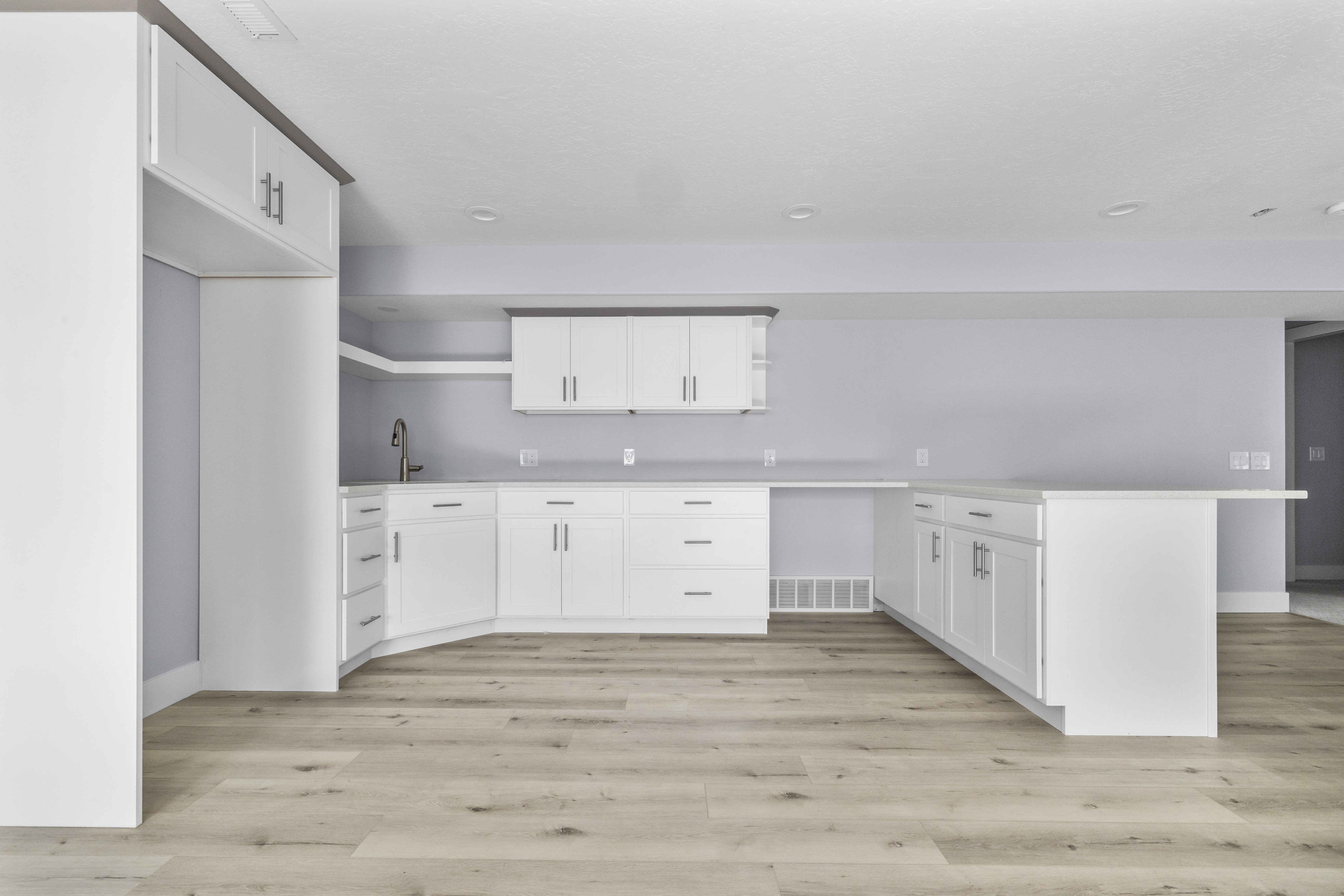 Modern kitchen in the basement featuring white cabinetry, light wood-finish flooring, a built-in refrigerator enclosure, a kitchen island, and a stainless steel faucet
