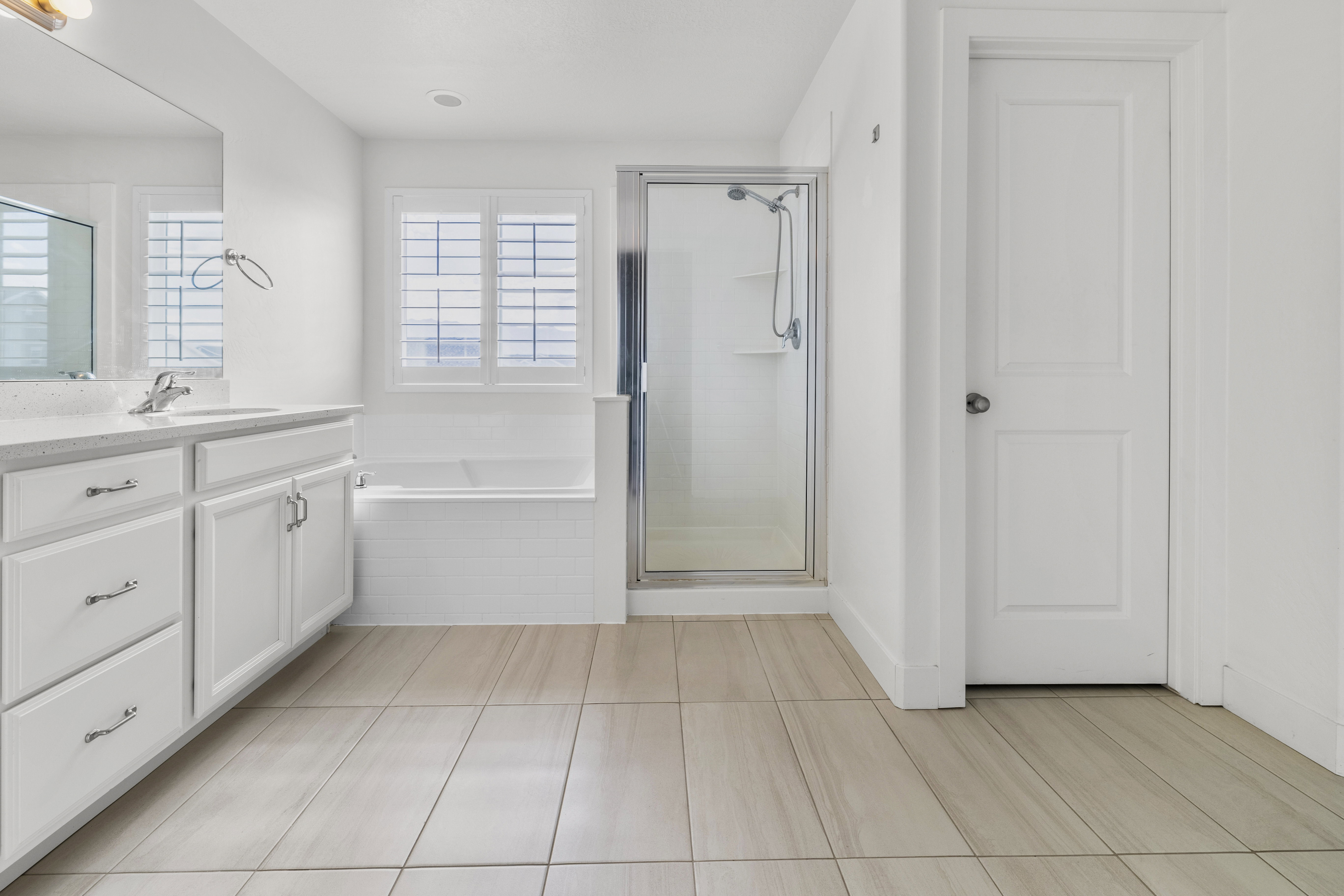 Primary bathroom. Bathroom featuring light-toned tile flooring, a white vanity with a light-colored countertop, and a built-in bathtub with subway tile surround