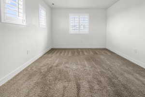 Bedroom 2. Bright room featuring two windows with white plantation shutters, white walls, and plush brown carpeting