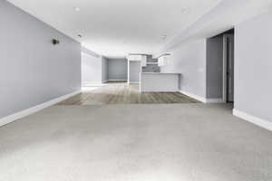 Open lower-level living space featuring light gray carpeting and light wood-finish flooring