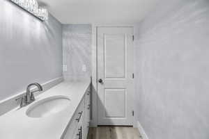 Bathroom vanity featuring an integrated sink, brushed nickel faucet, light-toned countertop, white cabinetry with dark hardware, and wood-finish flooring