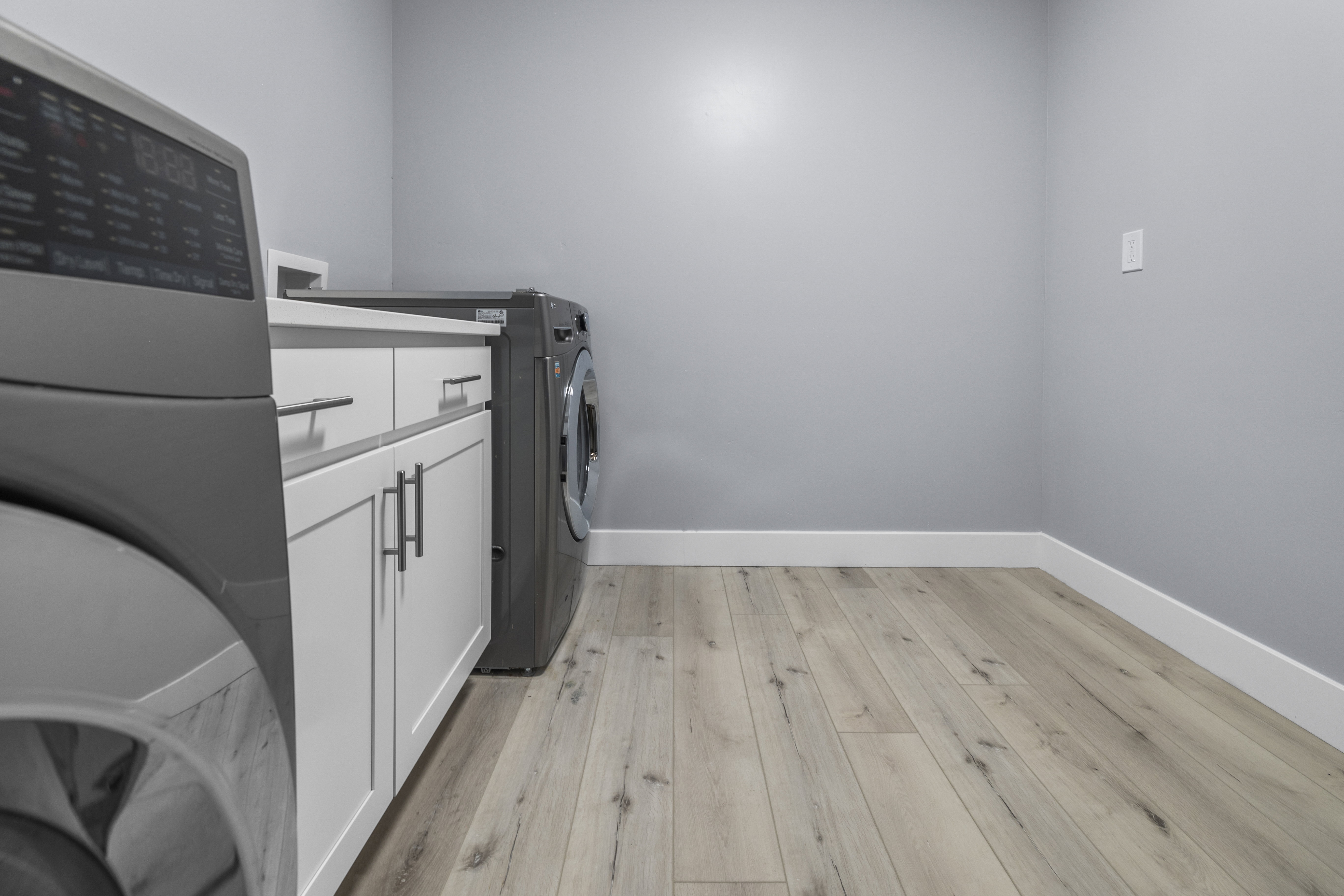 Dedicated laundry area in the basement featuring wood-finish flooring, light gray walls, white baseboards, and built-in cabinetry with a countertop
