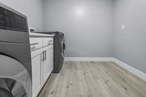 Dedicated laundry area in the basement featuring wood-finish flooring, light gray walls, white baseboards, and built-in cabinetry with a countertop