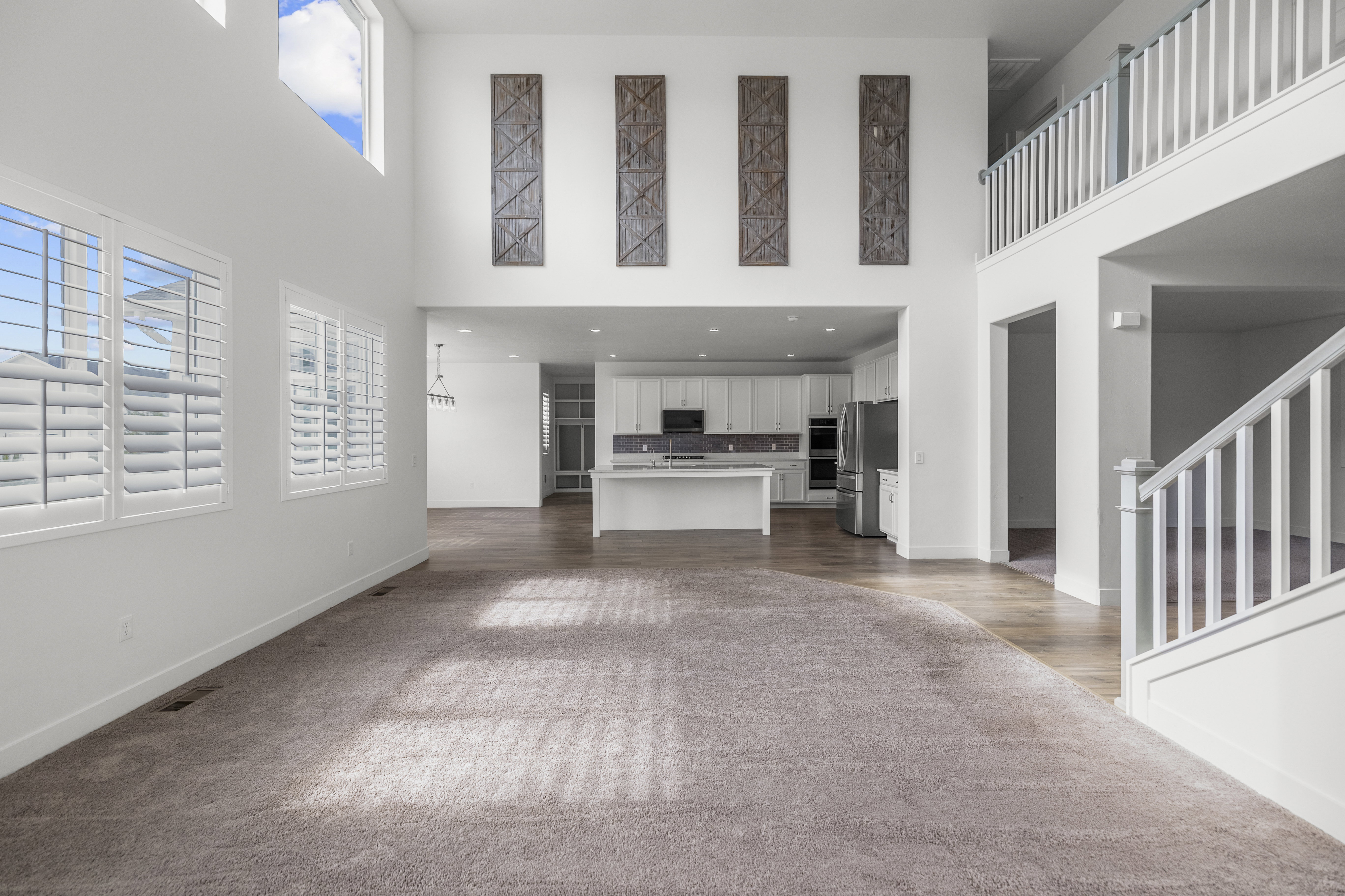 Spacious living area featuring high ceilings, white plantation shutters, and light-tone carpeting