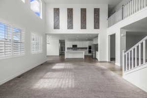 Spacious living area featuring high ceilings, white plantation shutters, and light-tone carpeting