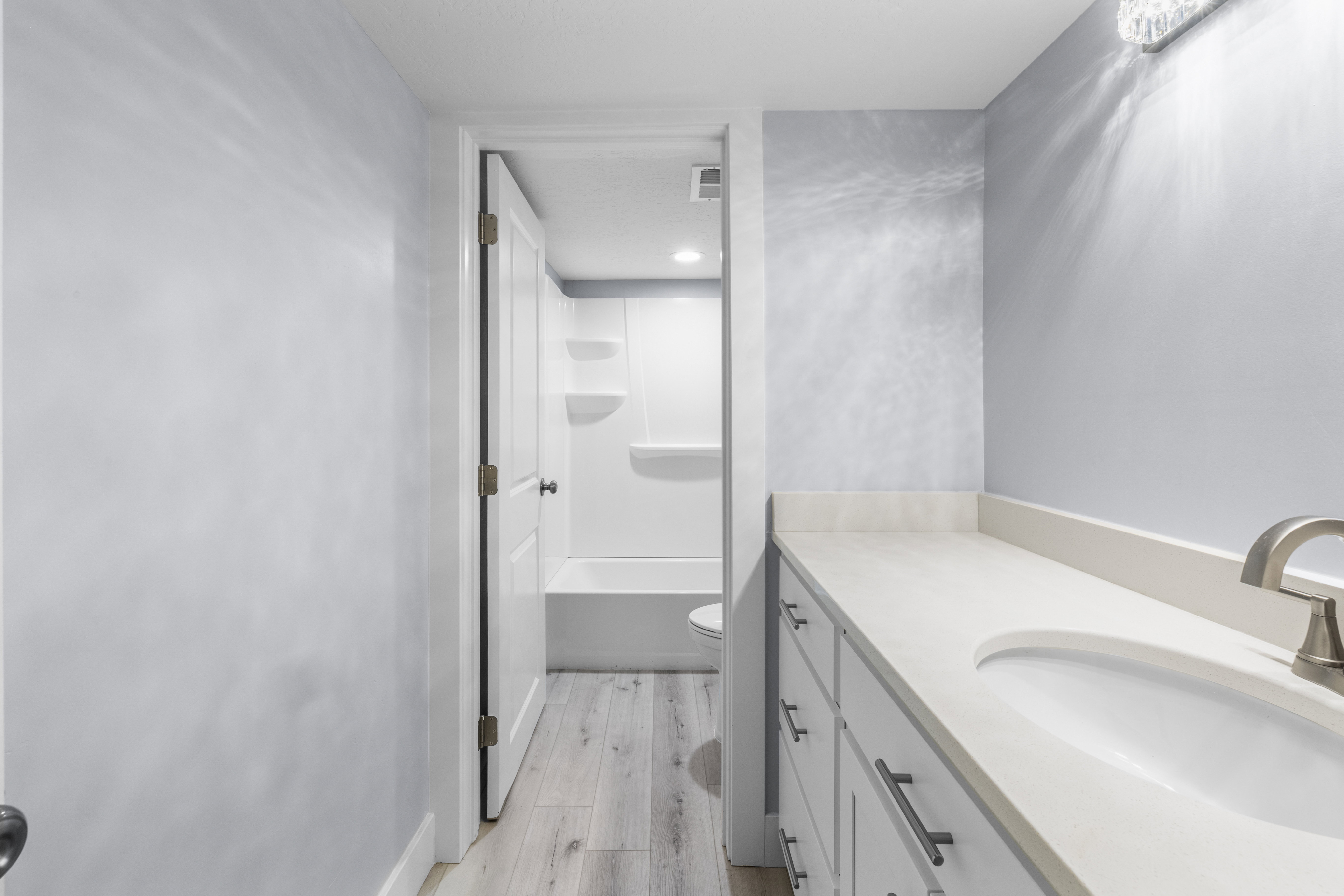 Bathroom vanity with light-toned countertop, undermount sink, and brushed nickel faucet