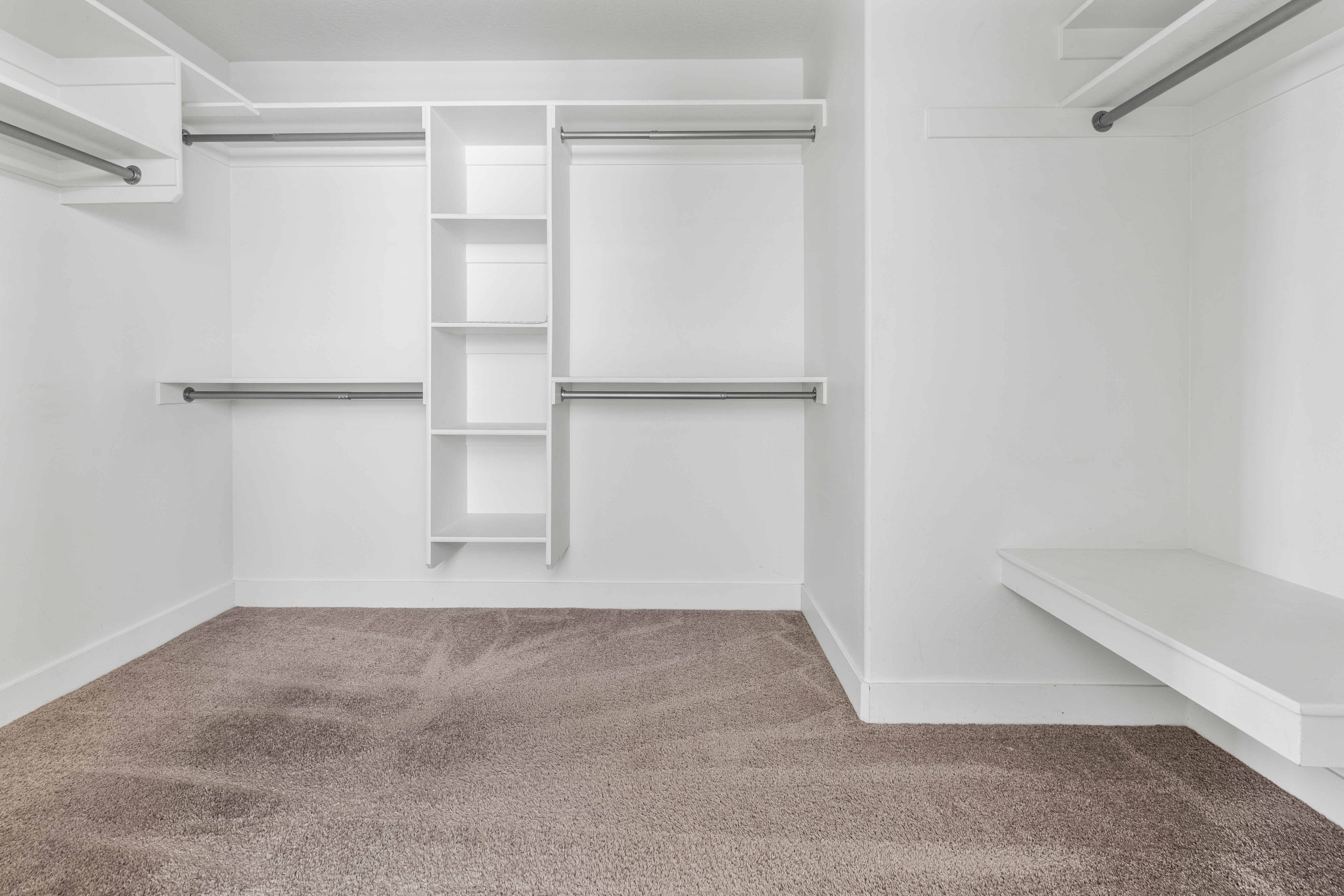 Primary Bedroom closet. Spacious walk-in closet featuring built-in shelving, multiple hanging rods, and a floating storage bench