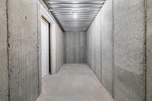 Cold storage space under the front porch in the basement featuring concrete slab flooring, poured concrete walls, exposed metal ceiling joists, and a white interior door frame