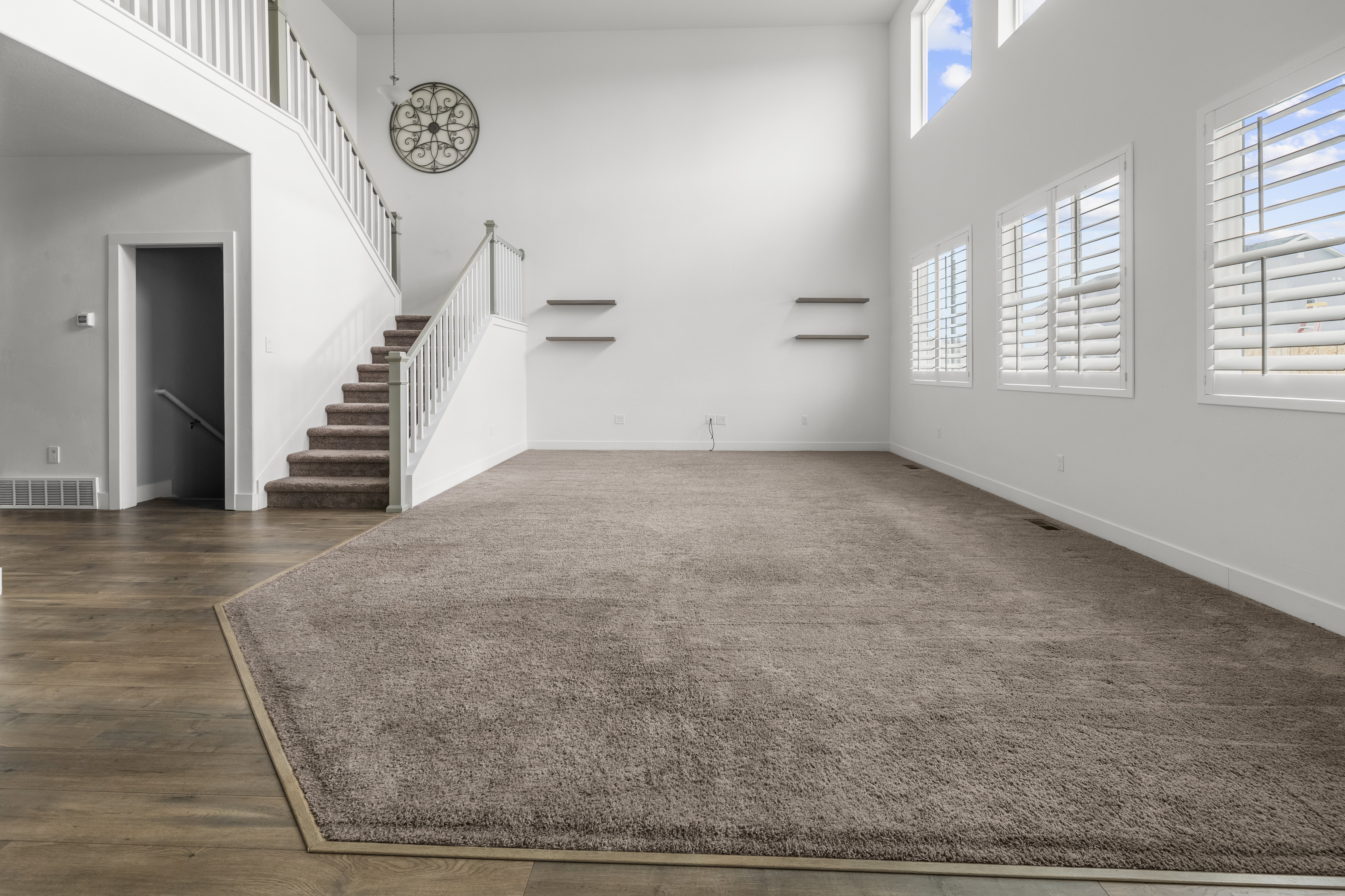 Two-story living area featuring a prominent staircase with white railings, wood-finish flooring, and a large carpeted area