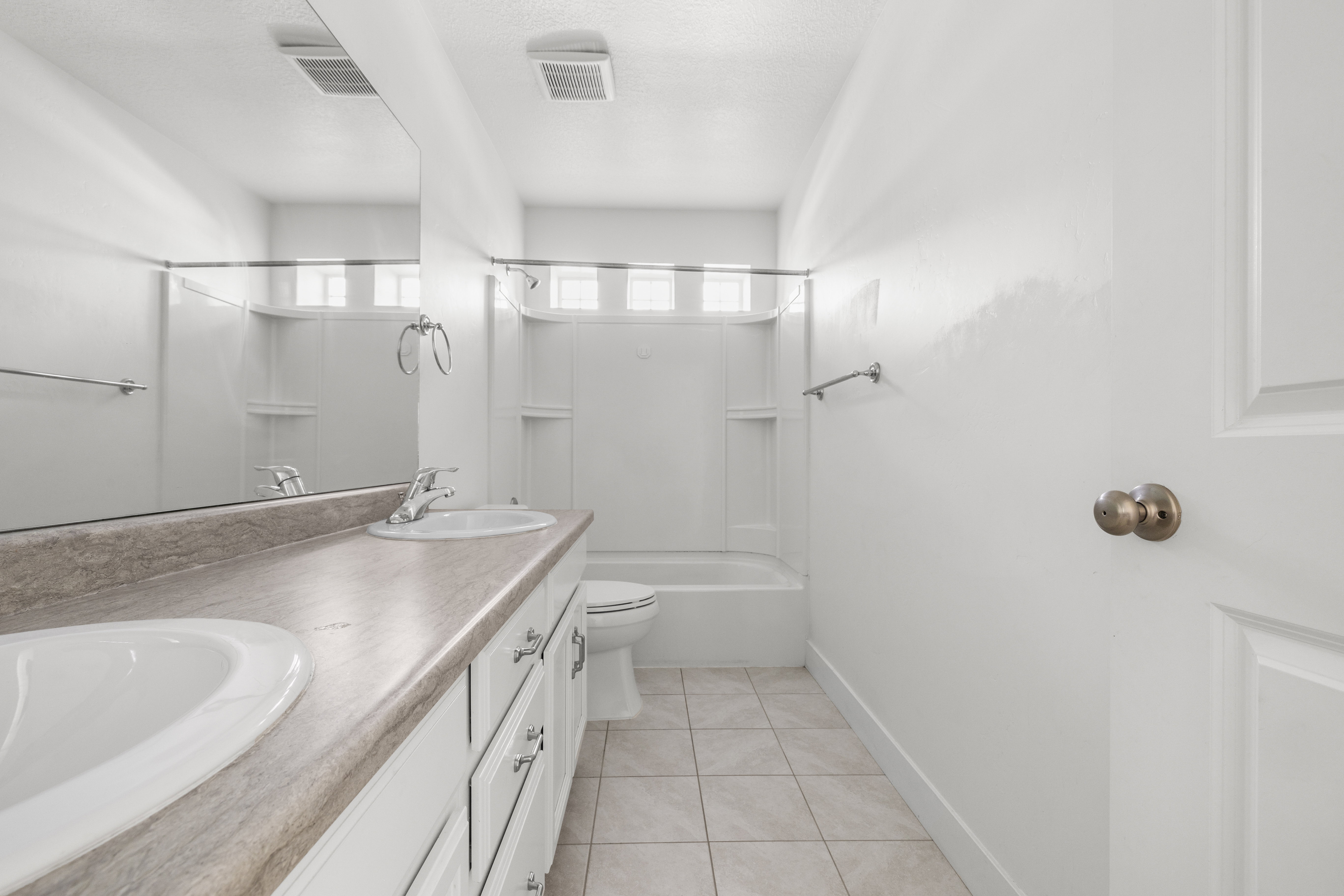 Bathroom featuring a double vanity with integrated sinks, a tub/shower combination, tiled flooring, and a large wall-mounted mirror