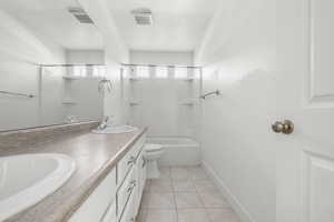 Bathroom featuring a double vanity with integrated sinks, a tub/shower combination, tiled flooring, and a large wall-mounted mirror