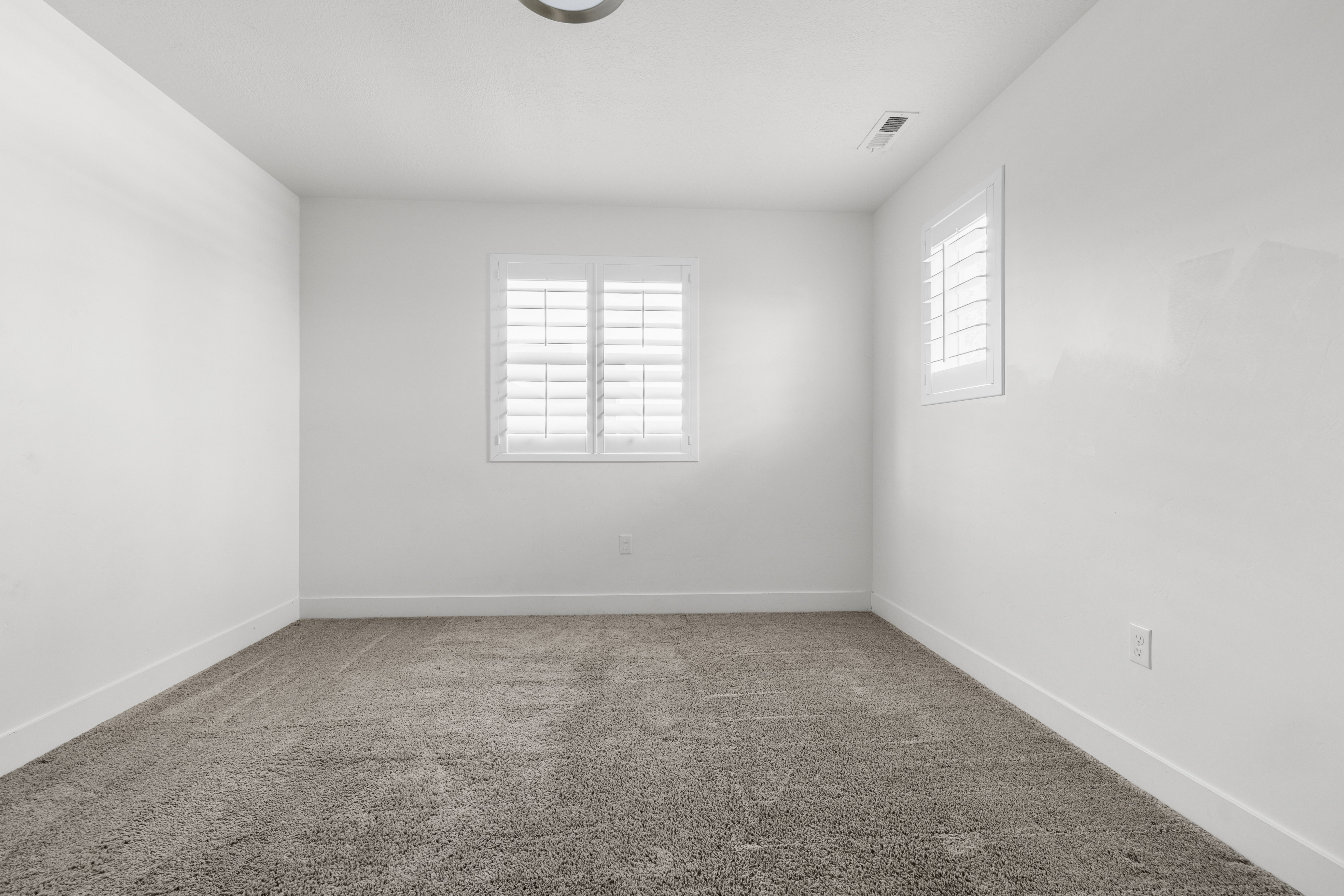 Bedroom 4. Carpeted interior with white walls, white trim, and two windows featuring plantation shutters