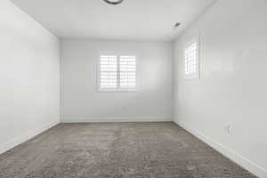 Bedroom 4. Carpeted interior with white walls, white trim, and two windows featuring plantation shutters