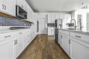 Kitchen featuring white cabinetry, wood-finish flooring, quartz-style countertops, and a blue subway tile backsplash