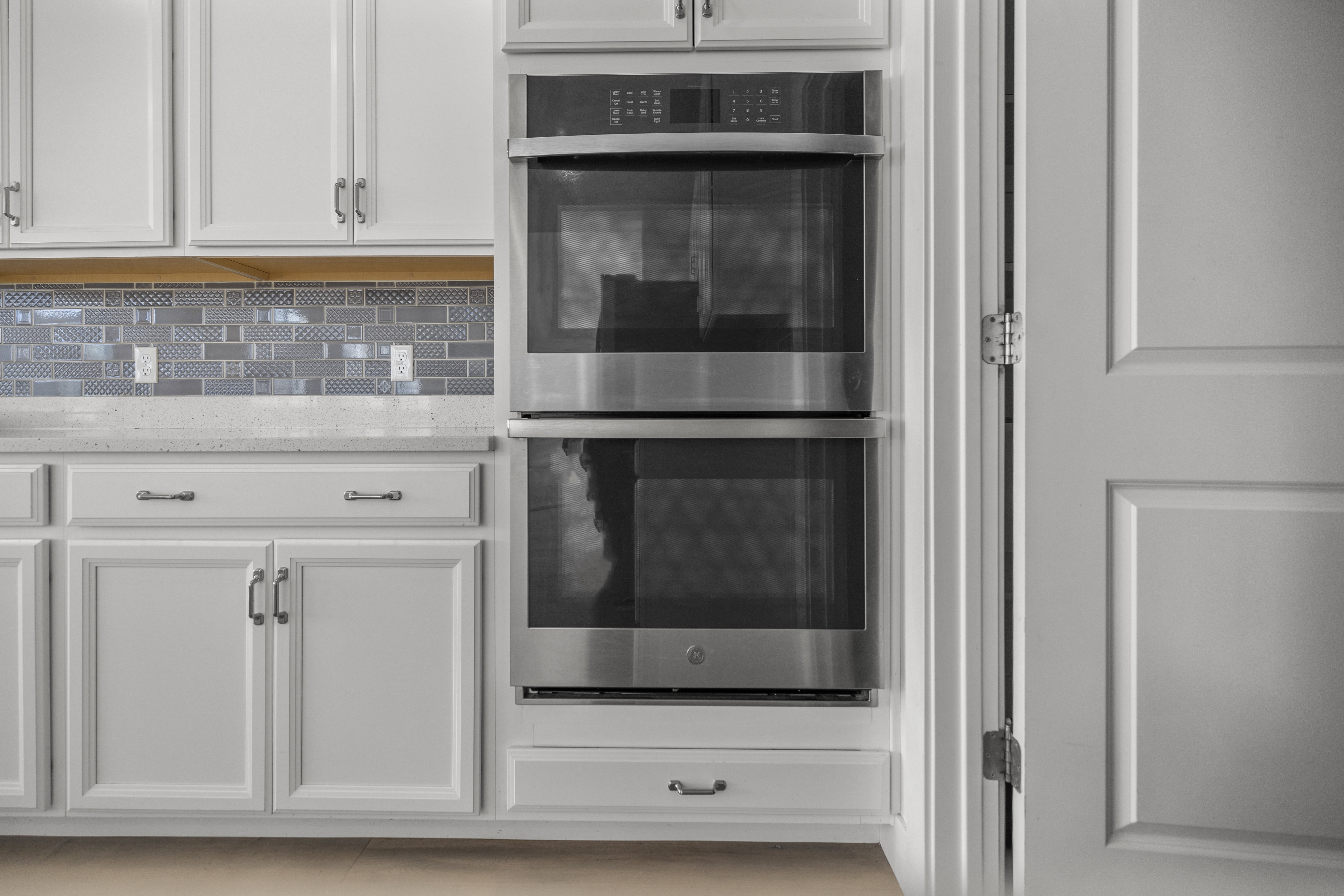 Stainless steel double wall ovens integrated into white cabinetry with matching cabinet hardware