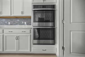 Stainless steel double wall ovens integrated into white cabinetry with matching cabinet hardware