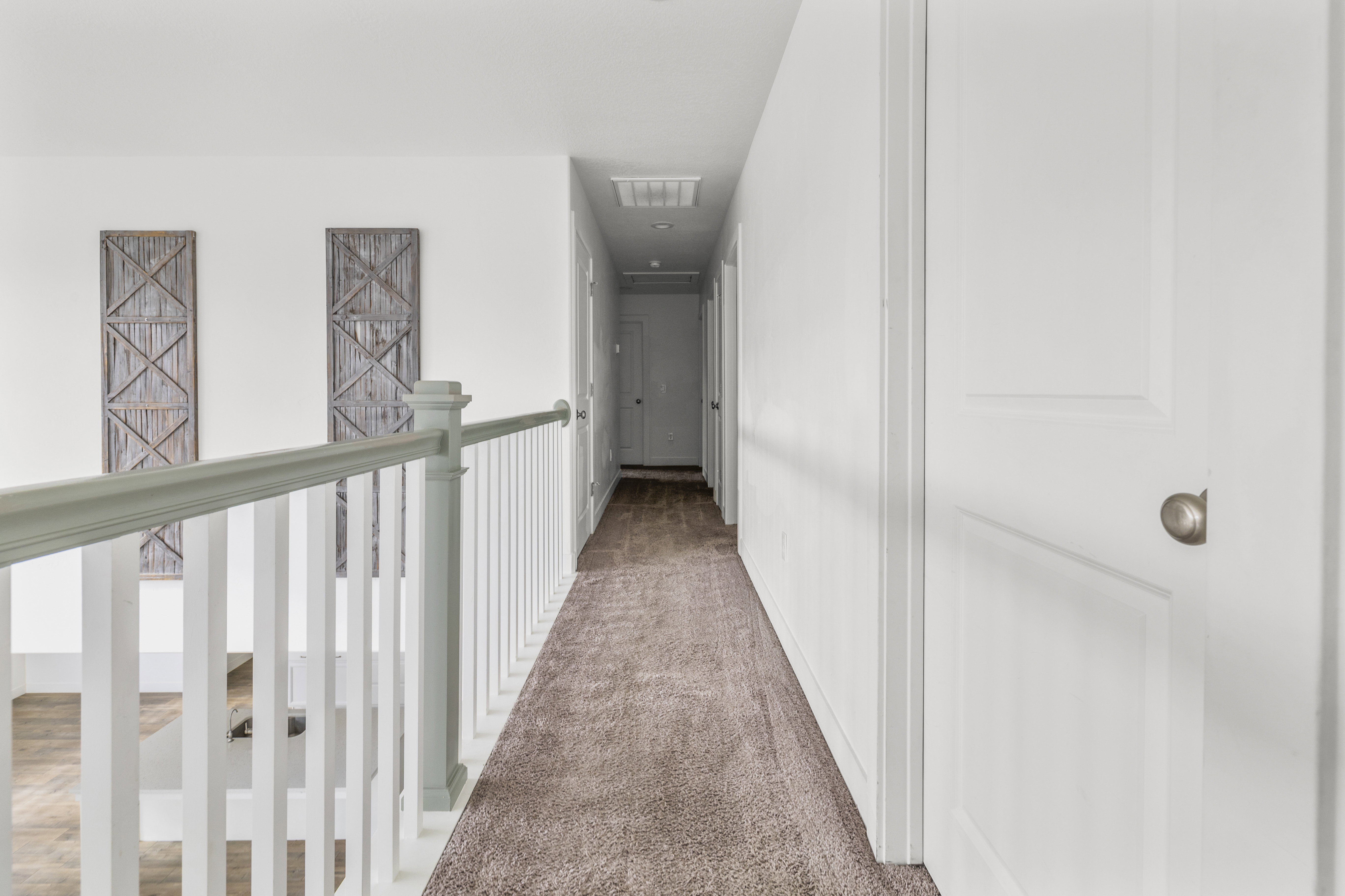 Second-story hallway featuring a carpeted floor, white walls, and a staircase railing with white spindles and a light-toned top rail