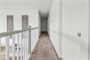 Second-story hallway featuring a carpeted floor, white walls, and a staircase railing with white spindles and a light-toned top rail