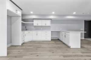 Contemporary kitchen area featuring white cabinetry, light-toned wood-finish flooring, recessed lighting, a built-in sink with a matte black faucet, and light-colored countertops